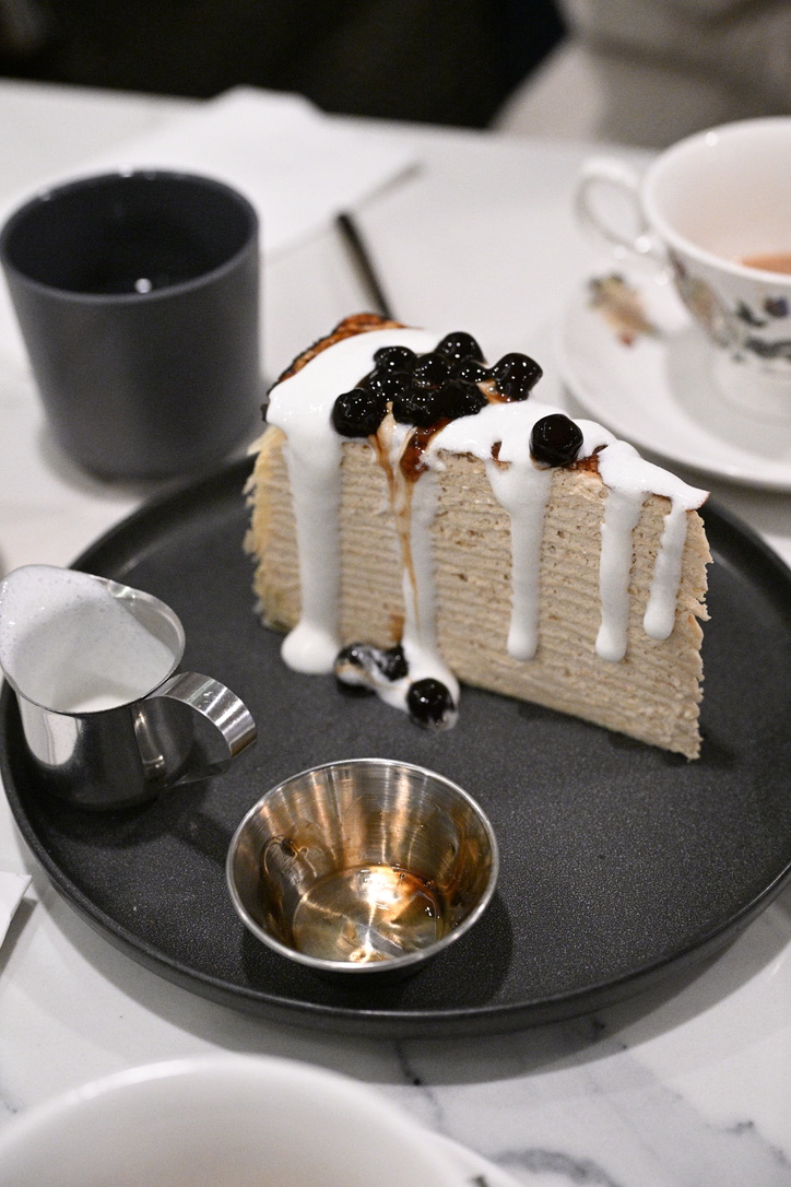 Slice of boba crepe cake with a cream drip beside a teacup